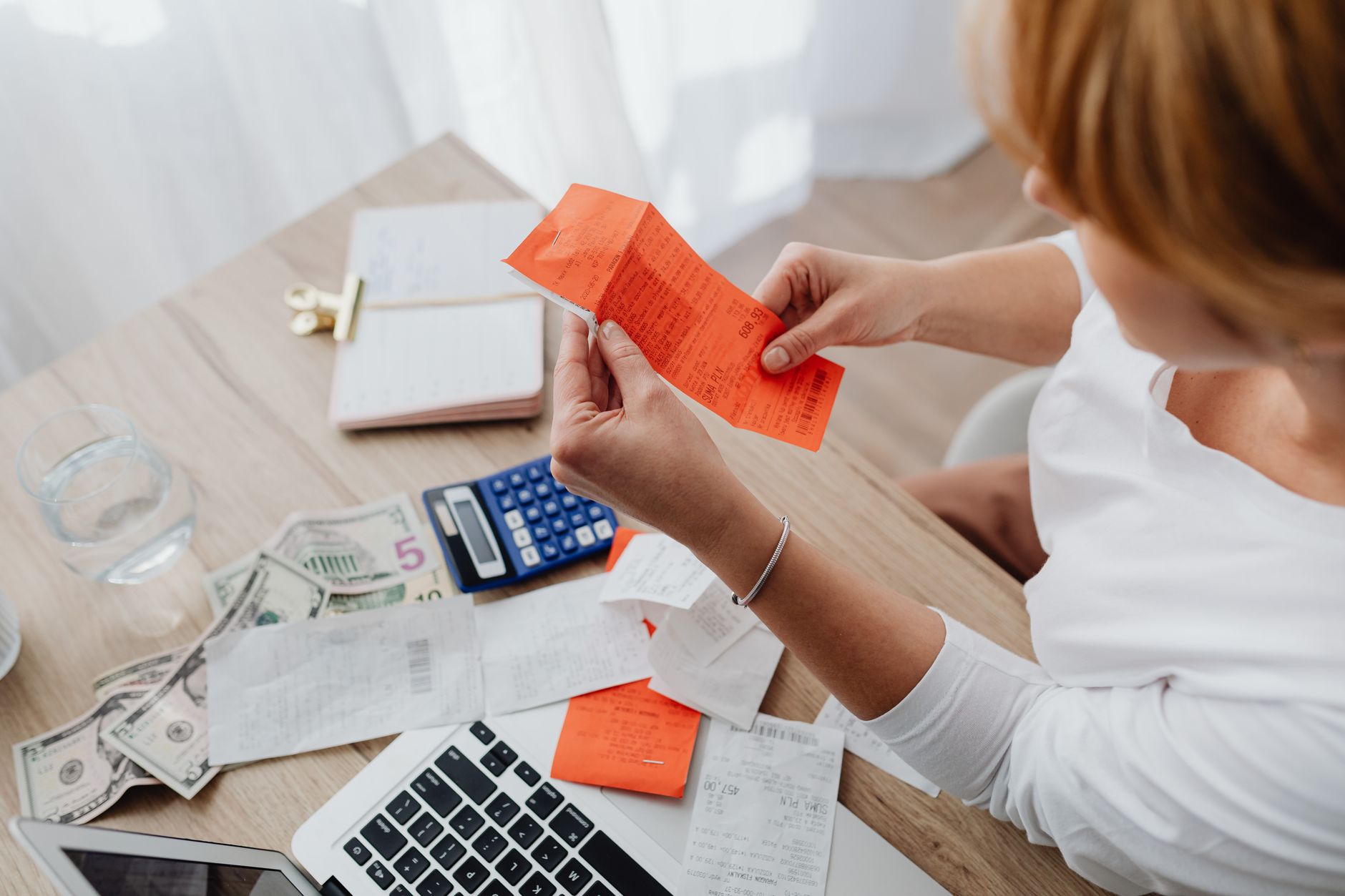 Nota fiscal avulsa: o que é e quem pode emitir Woman using calculator and receipts at home office desk for finance management.