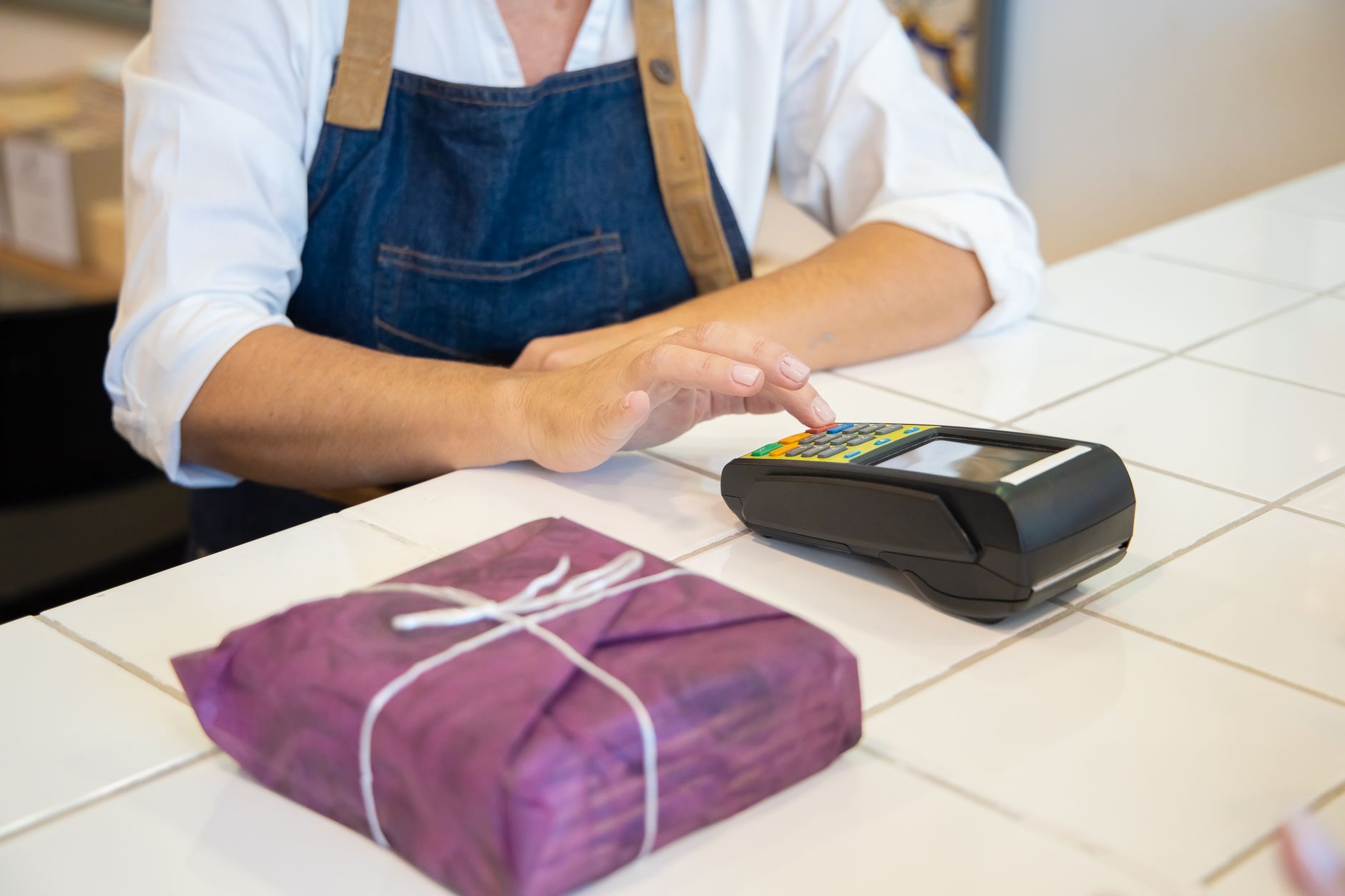 Nota fiscal avulsa para MEI: quando usar A person using contactless payment at a retail counter in Portugal wearing an apron.