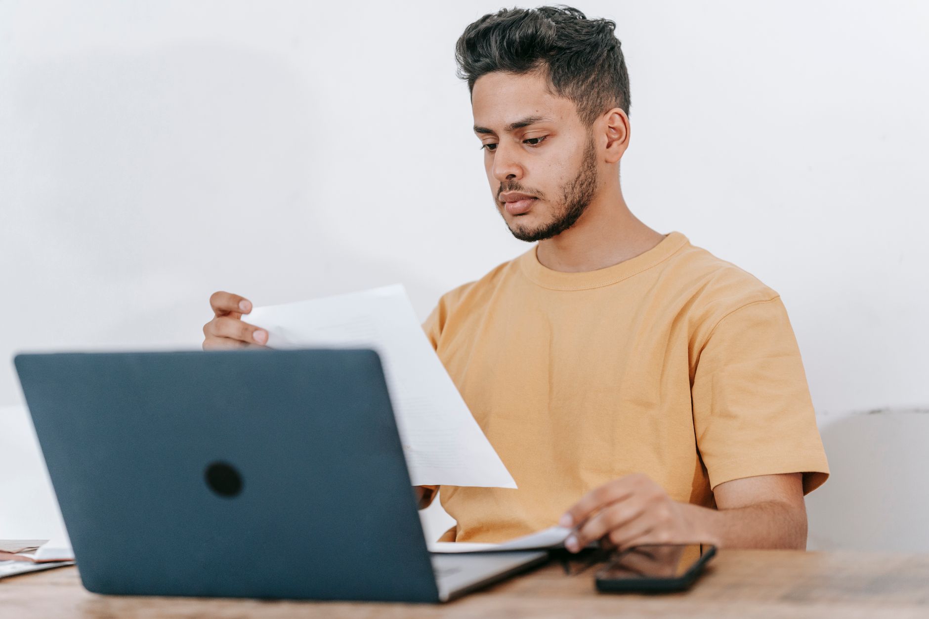 Portal de gestão da NFS-e: guia para o contribuinte Young bearded Hispanic male university student reading information on paper while studying online via laptop