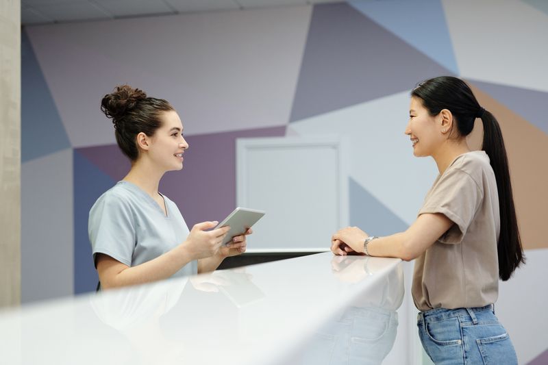 Anuidade do cartão pode ser negociada ou isentada? A receptionist and a visitor engaging at a modern reception desk, indoors.