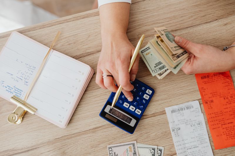 Cartão de loja ajuda ou atrapalha seu score? Hands managing finances with calculator, cash, and receipts on a wooden table. Ideal for budgeting concepts.