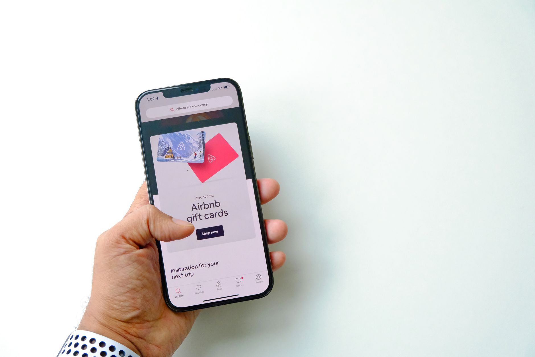 Cartão pré-pago recarregável: como funciona Close-up of a hand holding a smartphone displaying Airbnb gift cards on a white background.