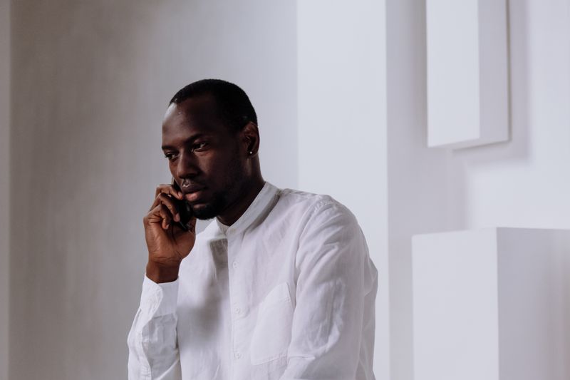 An African American man in a white shirt using a smartphone indoors, focused and serious.