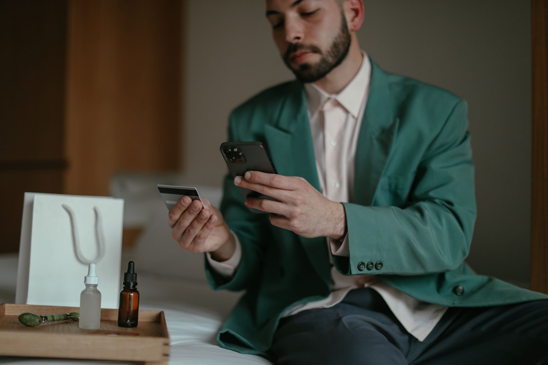 Man using smartphone and credit card for online shopping at home. Teal blazer and home setting create a relaxed feel.
