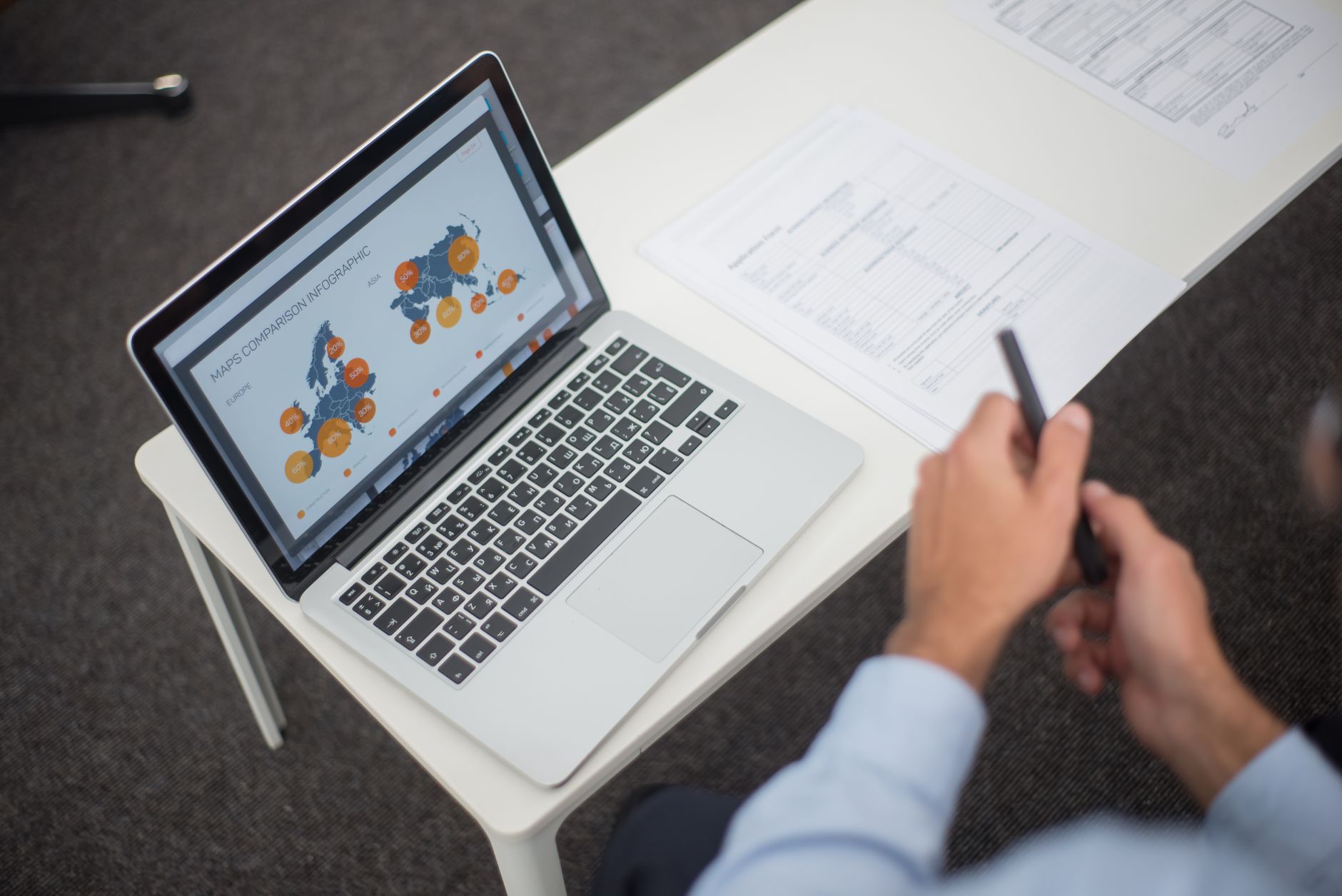 Como consultar suas dívidas em todos os bancos Professional analyzing data infographics on a laptop at an office desk, featuring documents and a pen.