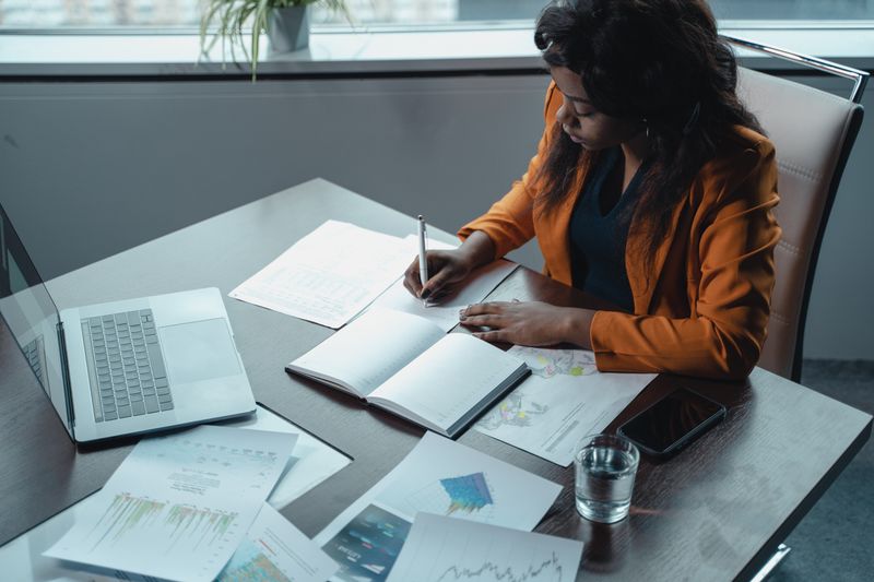 Como montar uma reserva de emergência com pouco dinheiro Businesswoman in office writing notes with documents and laptop, focused on analysis and productivity.