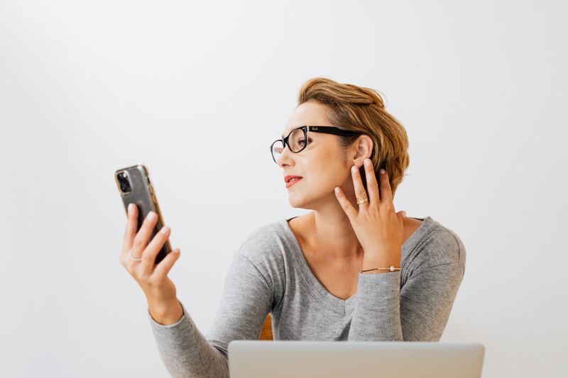 Consignado pelo celular: como contratar com segurança Caucasian woman with eyeglasses and light background taking a selfie indoors.