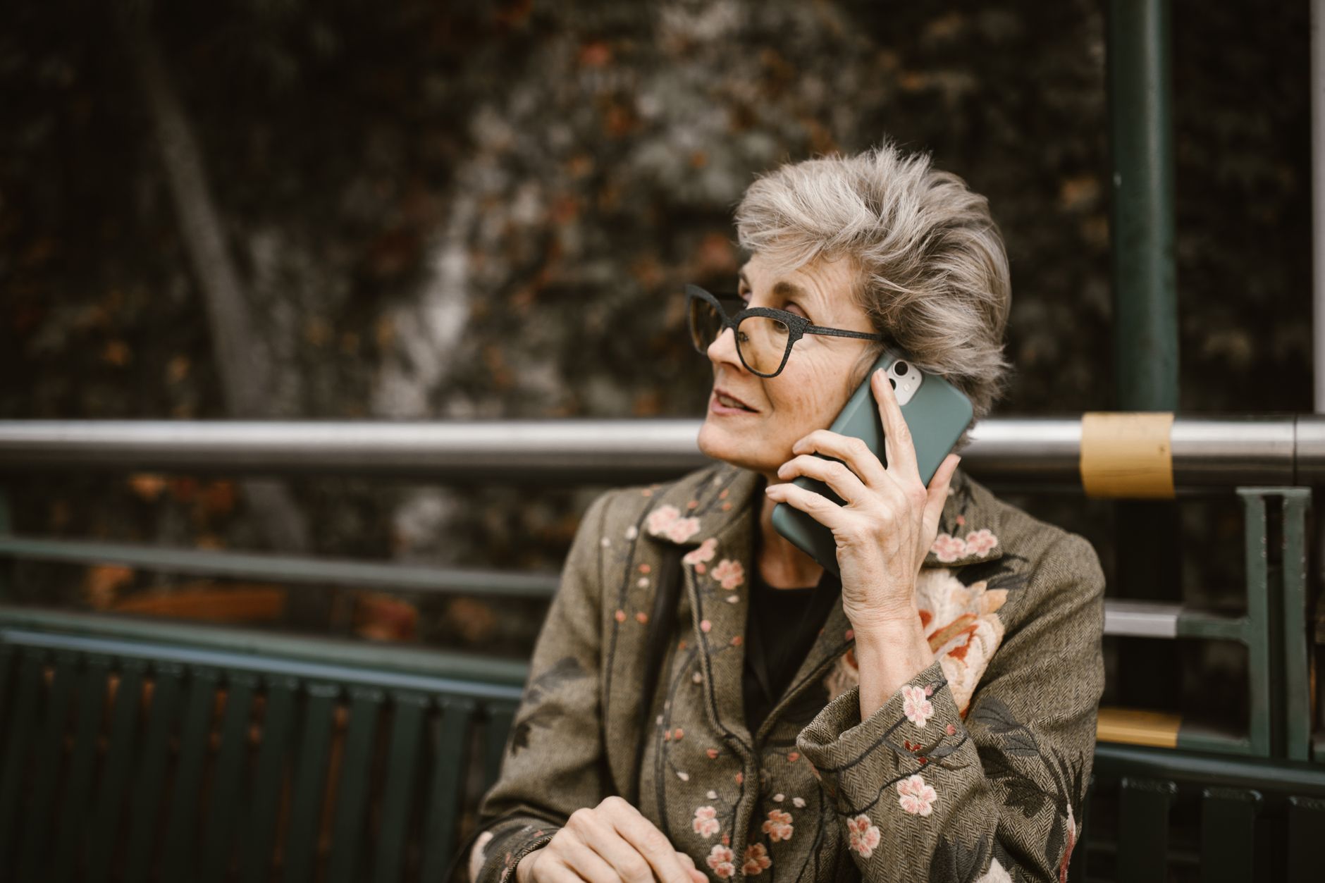 Consignado INSS: como funciona a taxa de juros Elderly woman with glasses talking on a smartphone while seated outdoors.