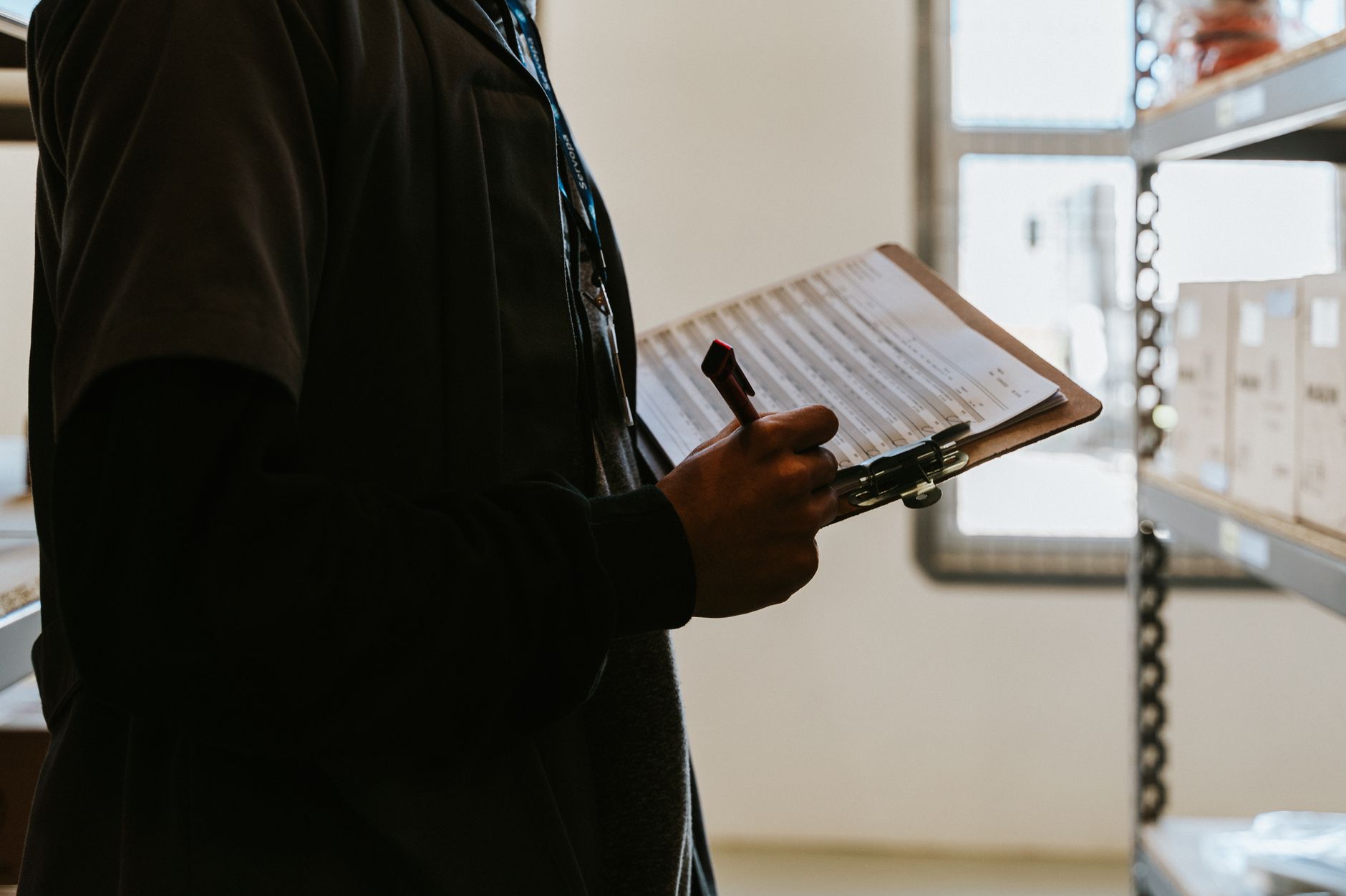 Estou no Serasa: ainda dá para fazer consignado? Industrial worker managing inventory in a warehouse with a clipboard and checklist.