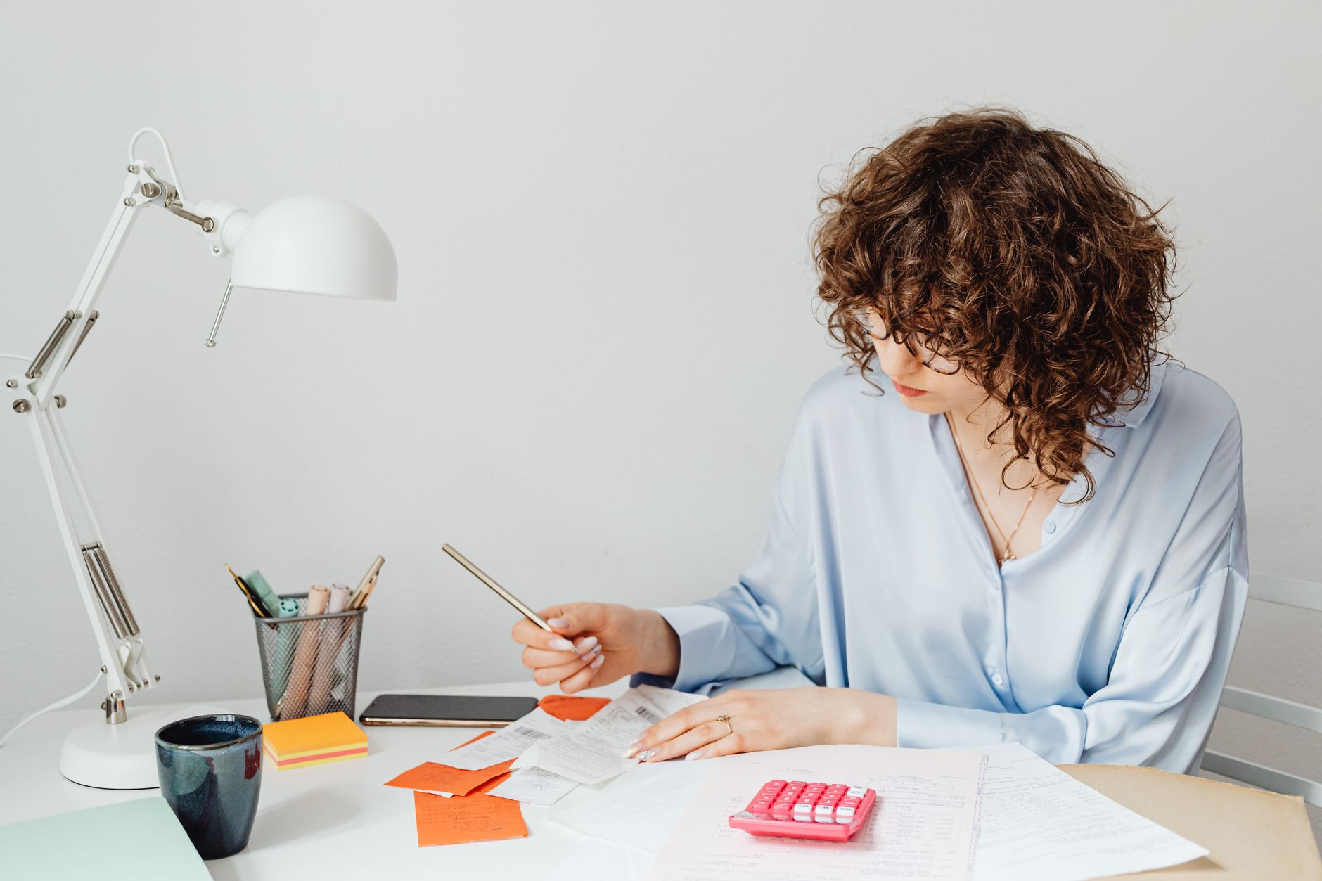 Consignado ou empréstimo pessoal: qual escolher Woman in office calculating expenses with documents, calculator, and coffee.