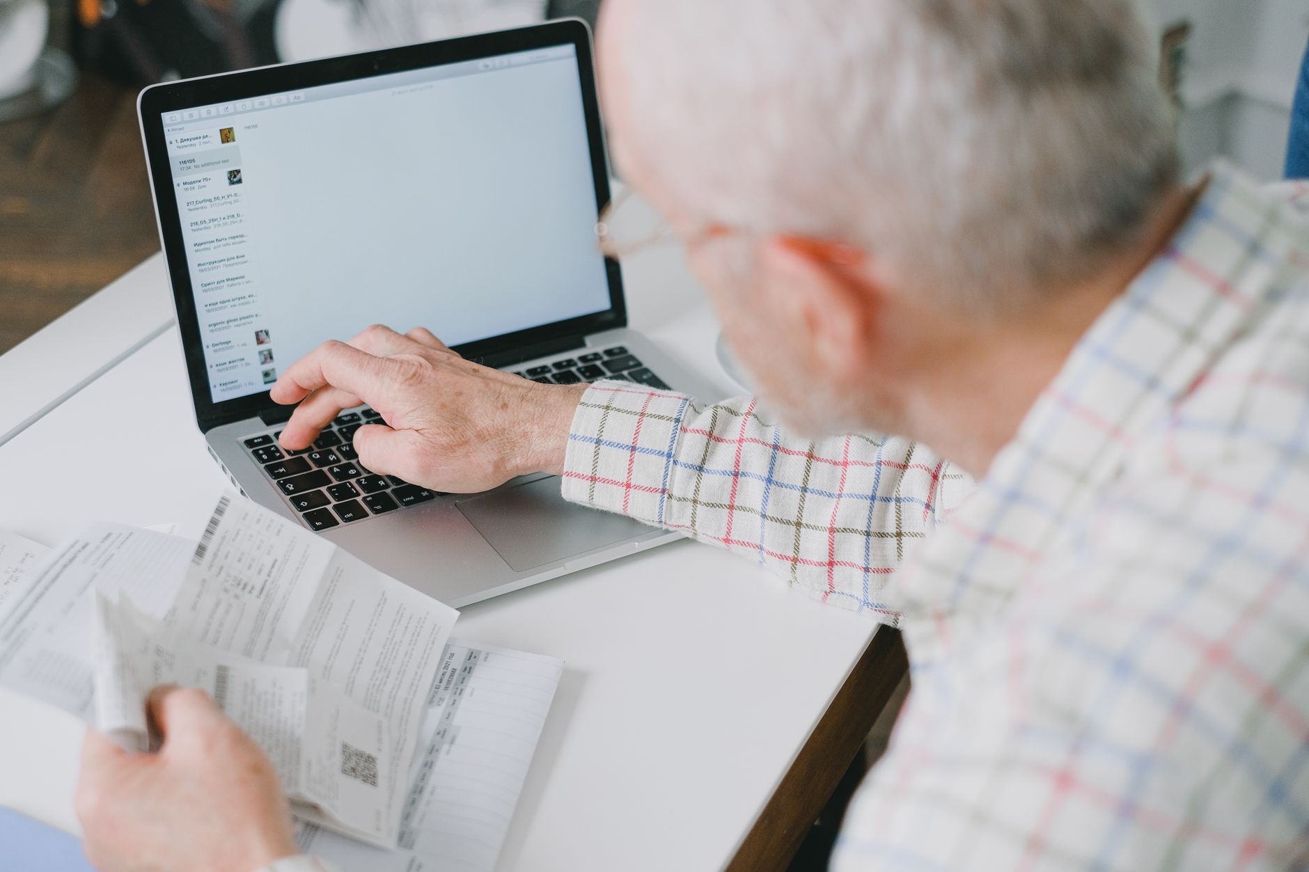 Desenrola Brasil: o que é e como participar Elderly man at desk handling finances online with documents and laptop.