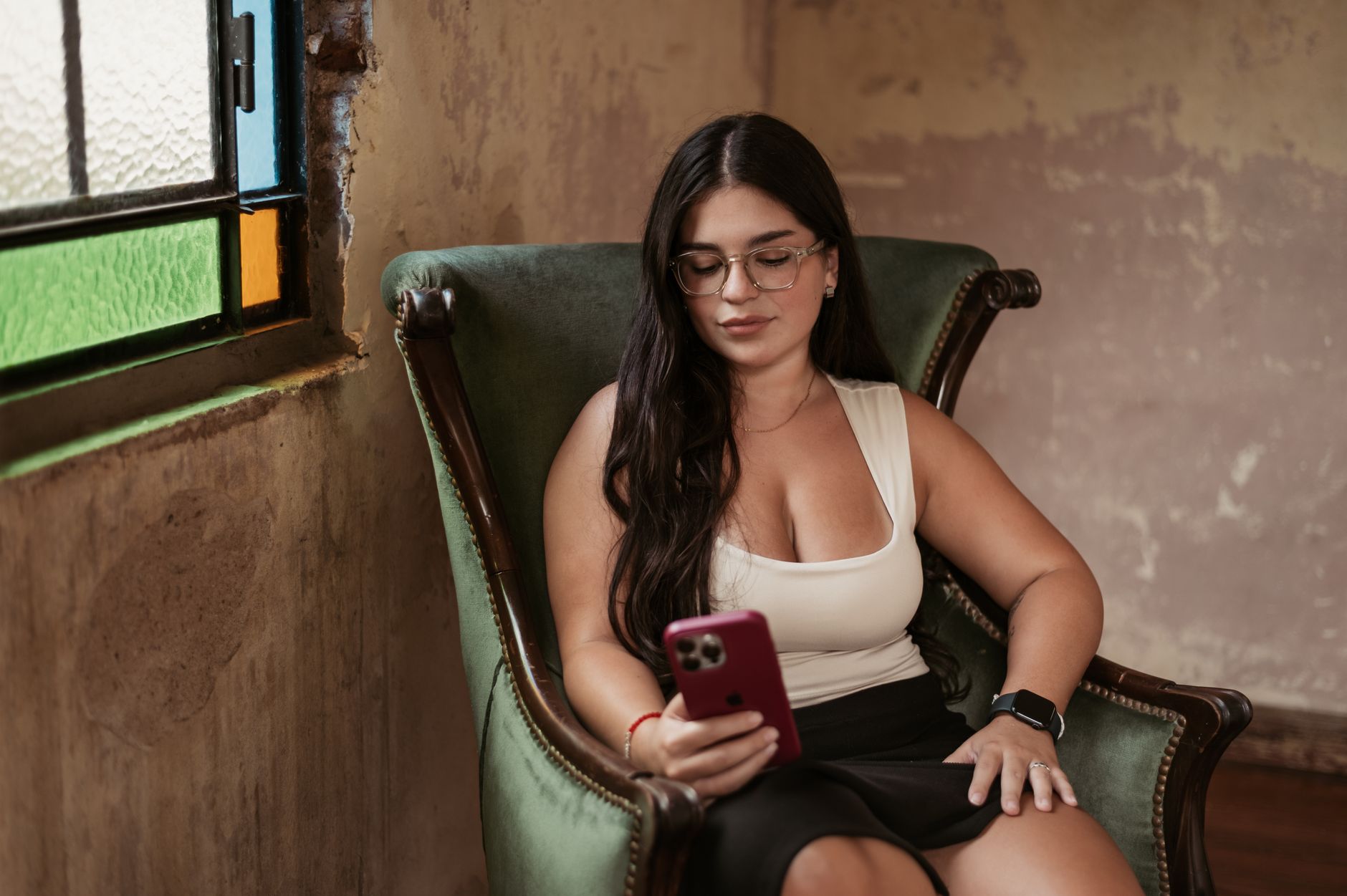 Sua dívida foi vendida para outra empresa: o que muda A young woman seated on a chair indoors, using her smartphone, showcasing relaxation and technology.