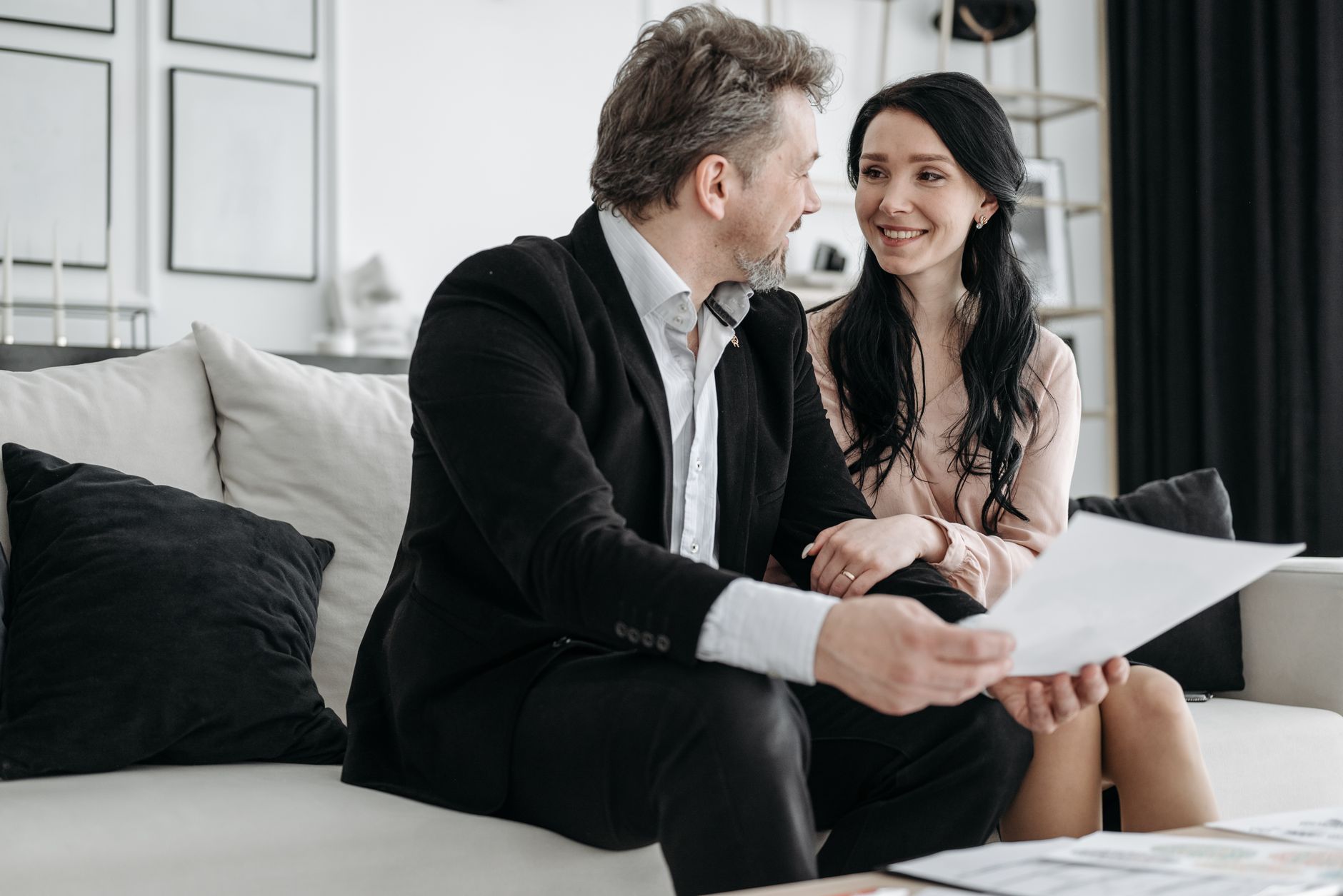 Empréstimo para dona de casa negativada: o que avaliar Couple smiling while sitting on a couch reviewing documents indoors.