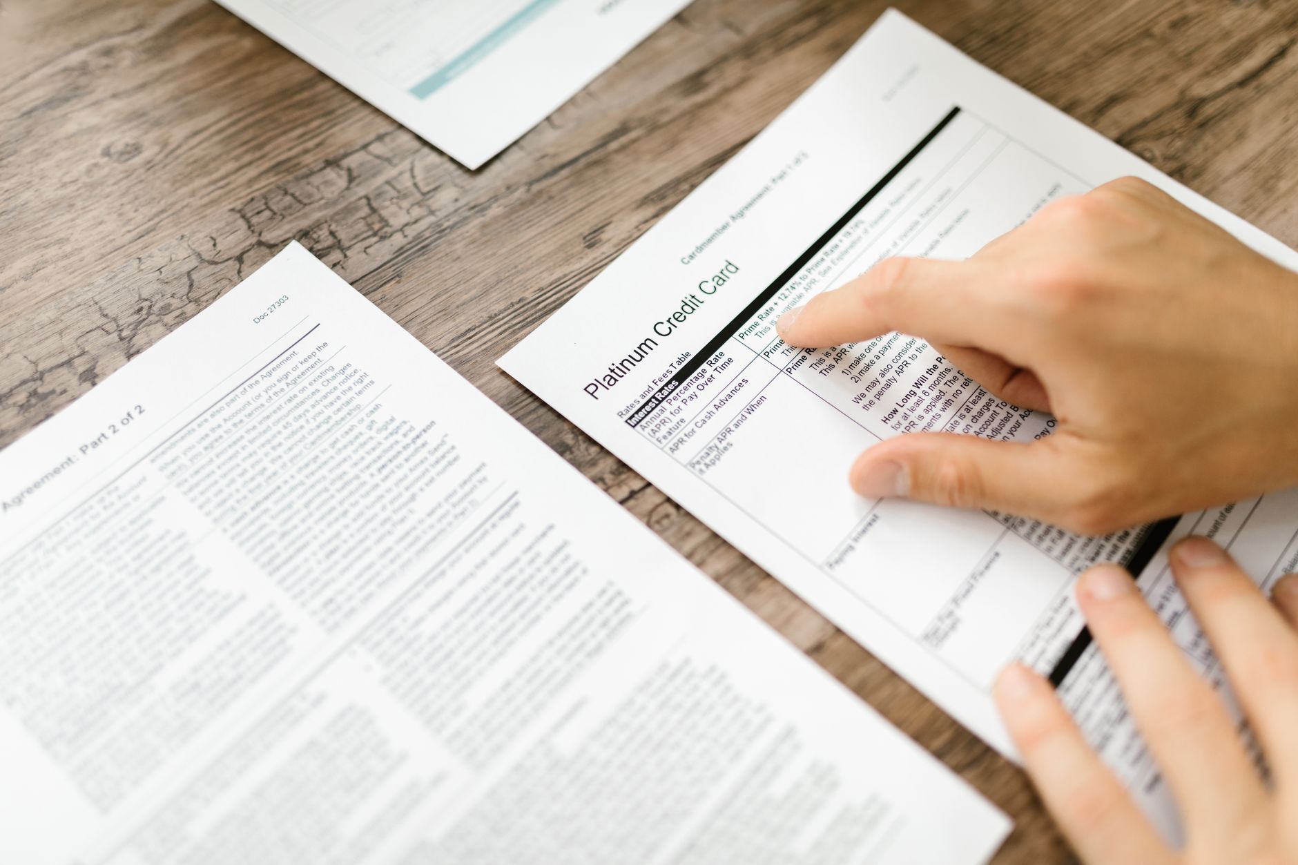 Empréstimo para quem tem cheque sem fundos: o que avaliar A hand examining a credit card agreement on a wooden desk, highlighting financial review.
