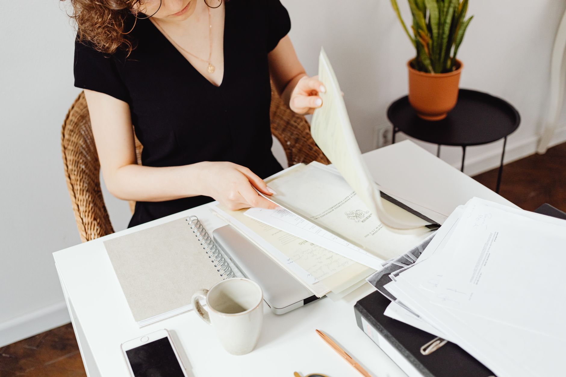 Empréstimo para negativado: como conseguir valor maior Woman sorting through documents in a home office setting. Organized workspace with plants.