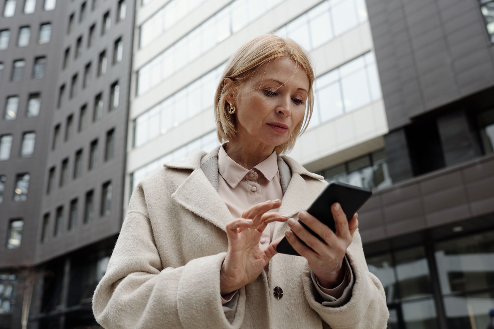 Empréstimo para idoso negativado: consignado é opção? Woman in coat using smartphone in front of modern building. Professional and focused expression.