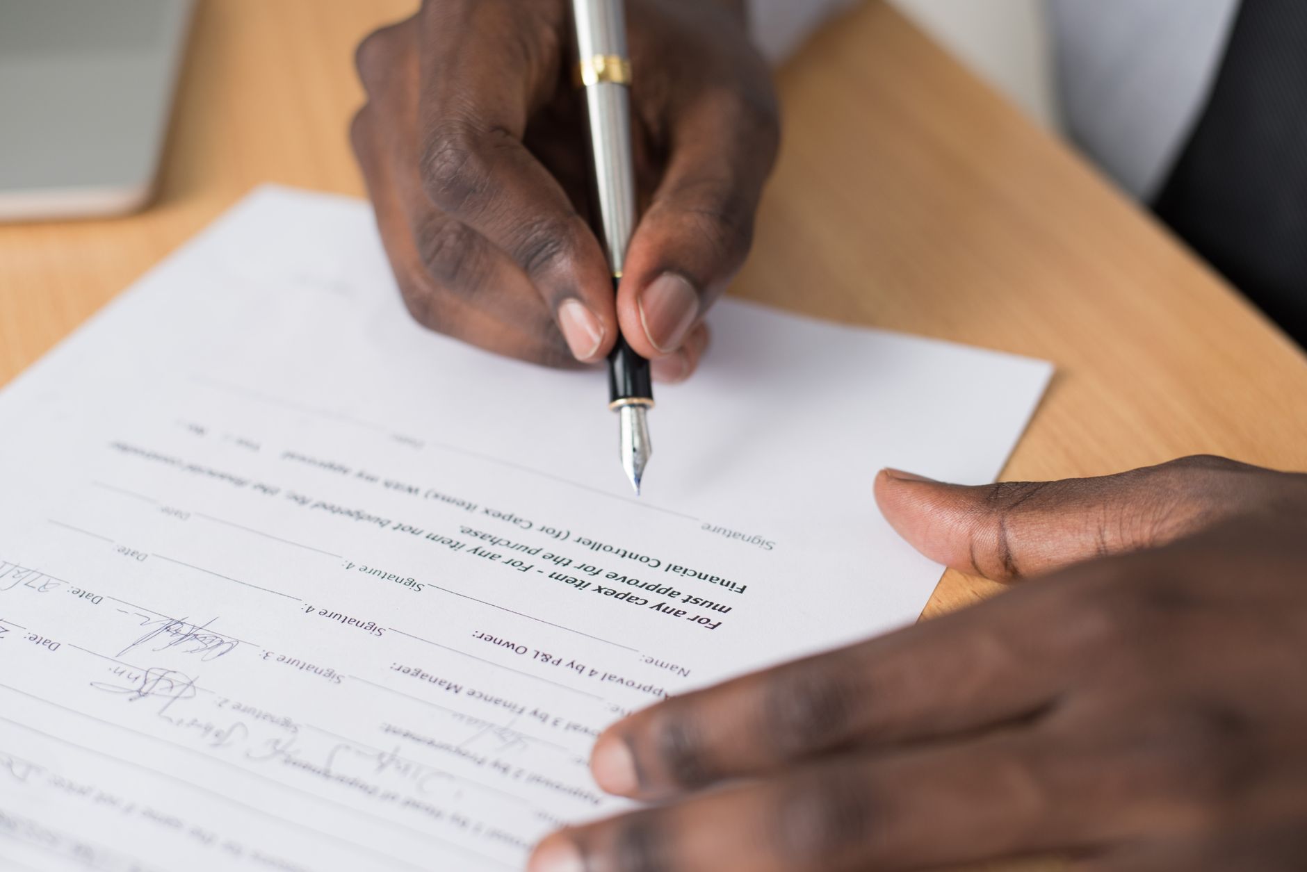 Empréstimo pessoal online: definição e funcionamento Close-up of a man's hands signing a formal document indoors.