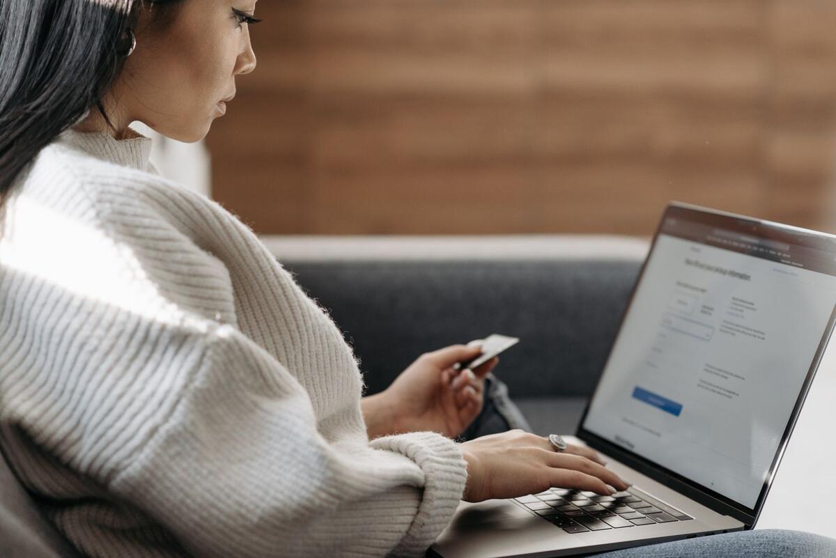 IPVA atrasado suja o nome? Mulher no sofá pagando contas pela internet com notebook e cartão