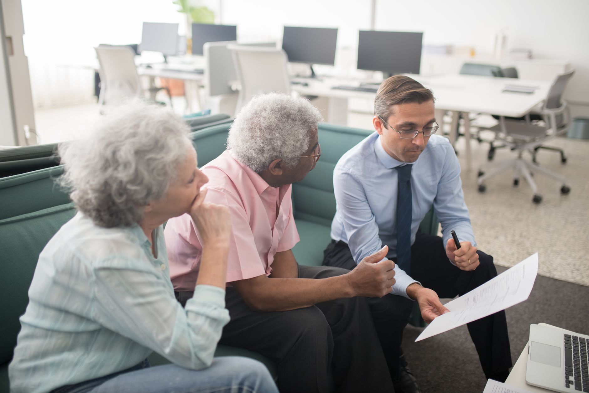 Existe limite de idade para consignado do INSS? Business professional consults elderly clients in an office setting. Collaborative discussion, paperwork visible.