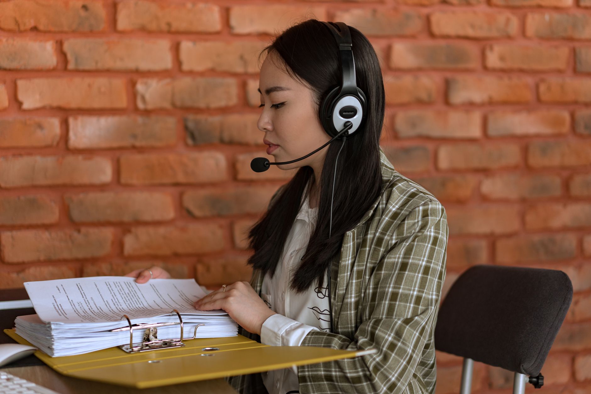 Negativação indevida: o que fazer quando você não deve An Asian woman working in an office, wearing headphones and reviewing documents.
