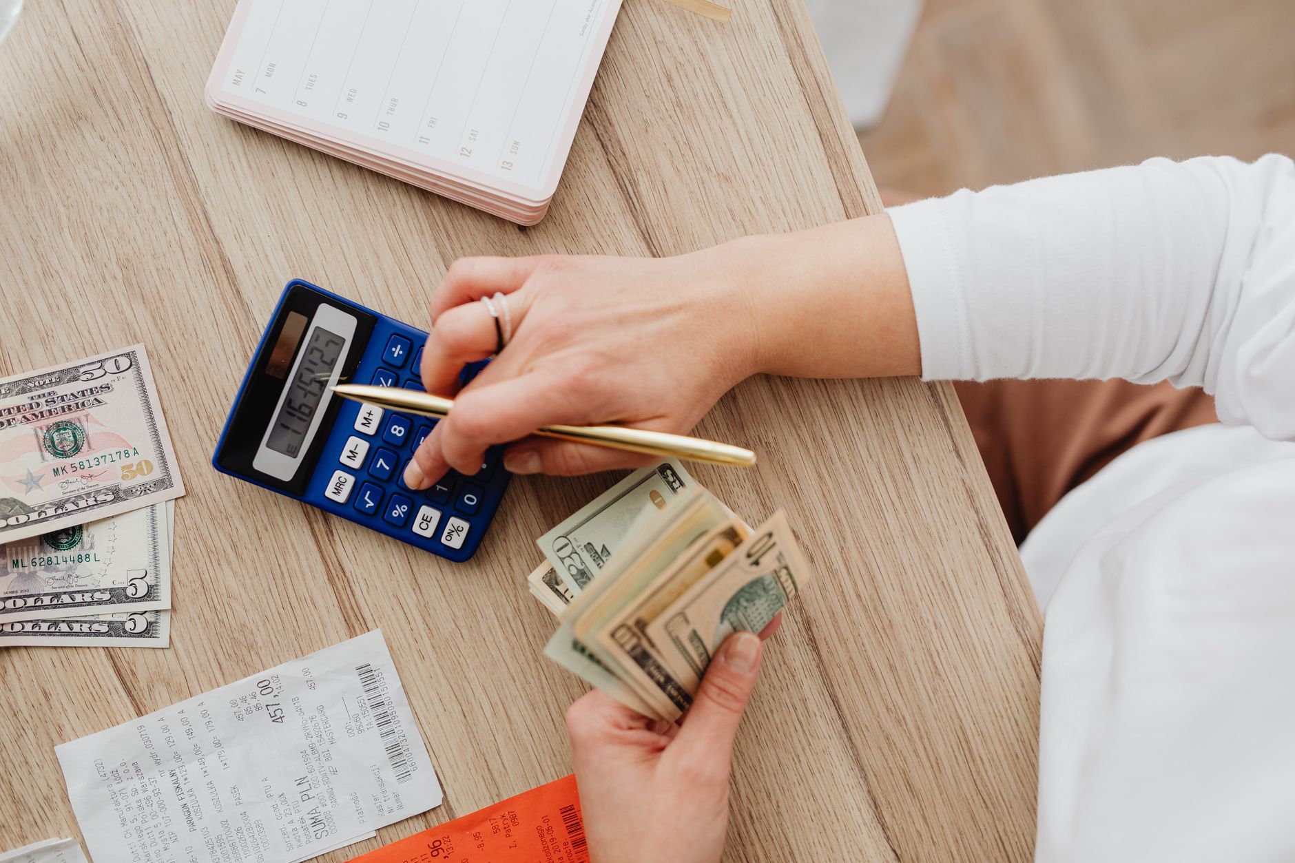 CET: o número que mostra o custo real de um empréstimo Person using a calculator and counting cash on a wooden table with receipts.