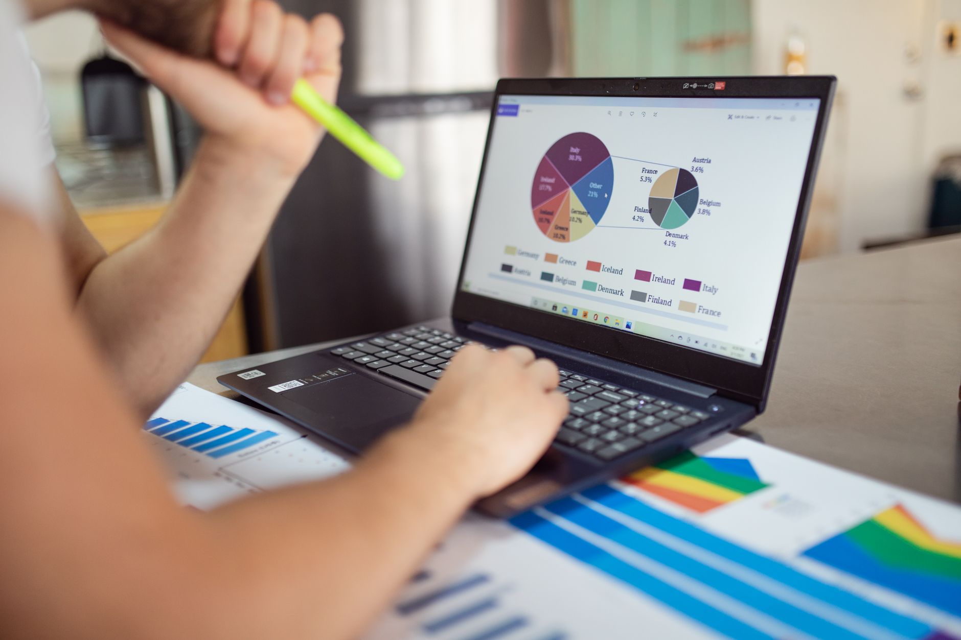 O que é score de crédito e como ele é calculado Person analyzing financial charts and graphs on a laptop with colorful documents, showcasing market analysis.