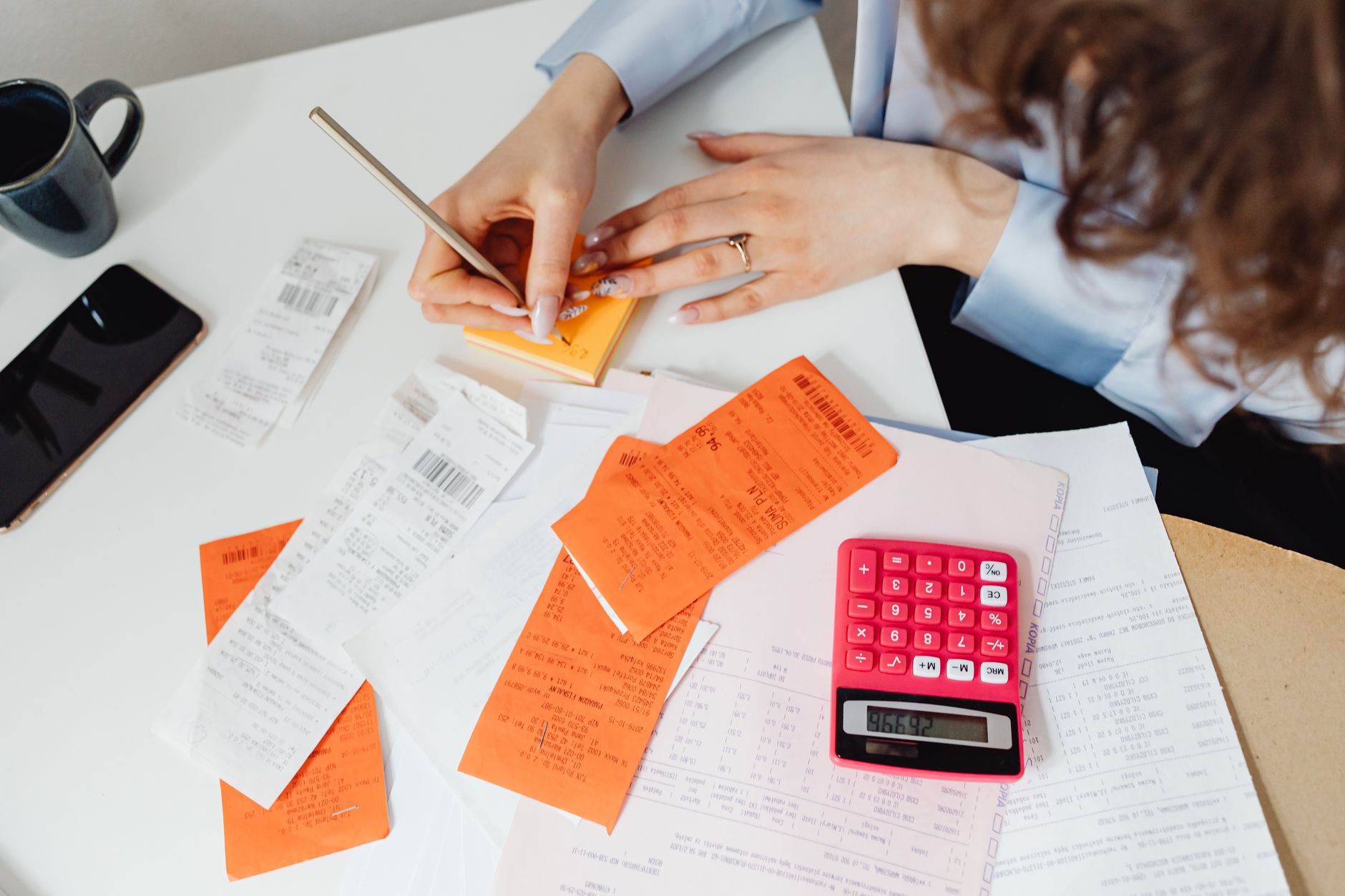 Pessoa organizando contas e anotações financeiras em uma mesa de casa.