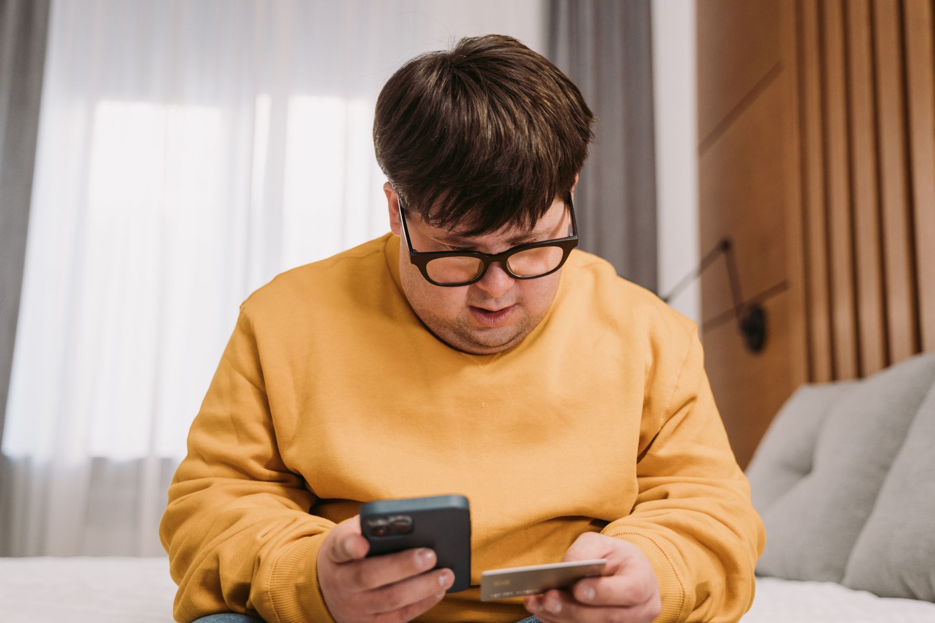 Programas de renegociação dos bancos: onde encontrar Man in yellow sweater using smartphone and credit card for online shopping indoors.