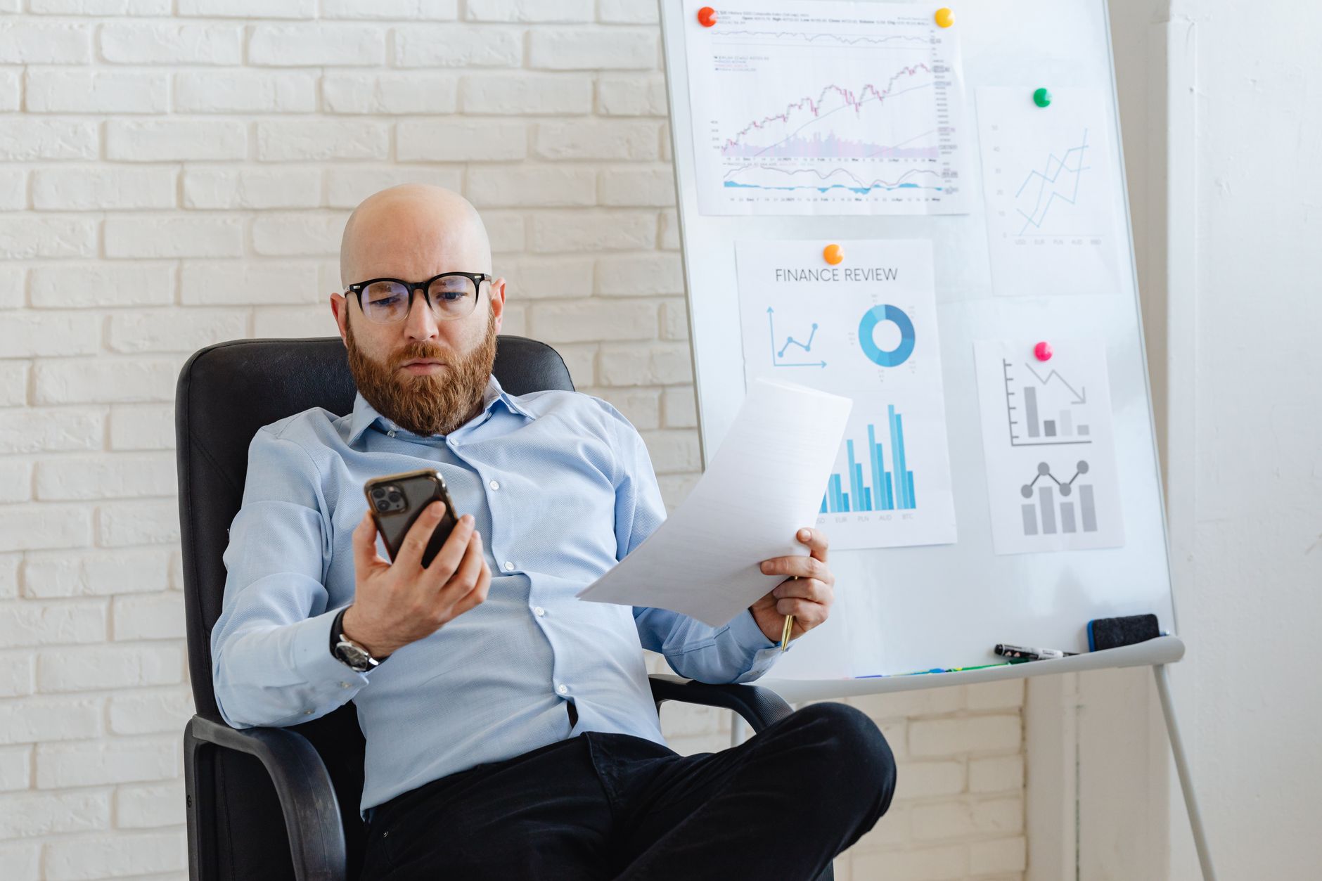 Quanto o score influencia na taxa de juros do crédito Bald businessman in corporate attire reviewing paperwork and smartphone data indoors.