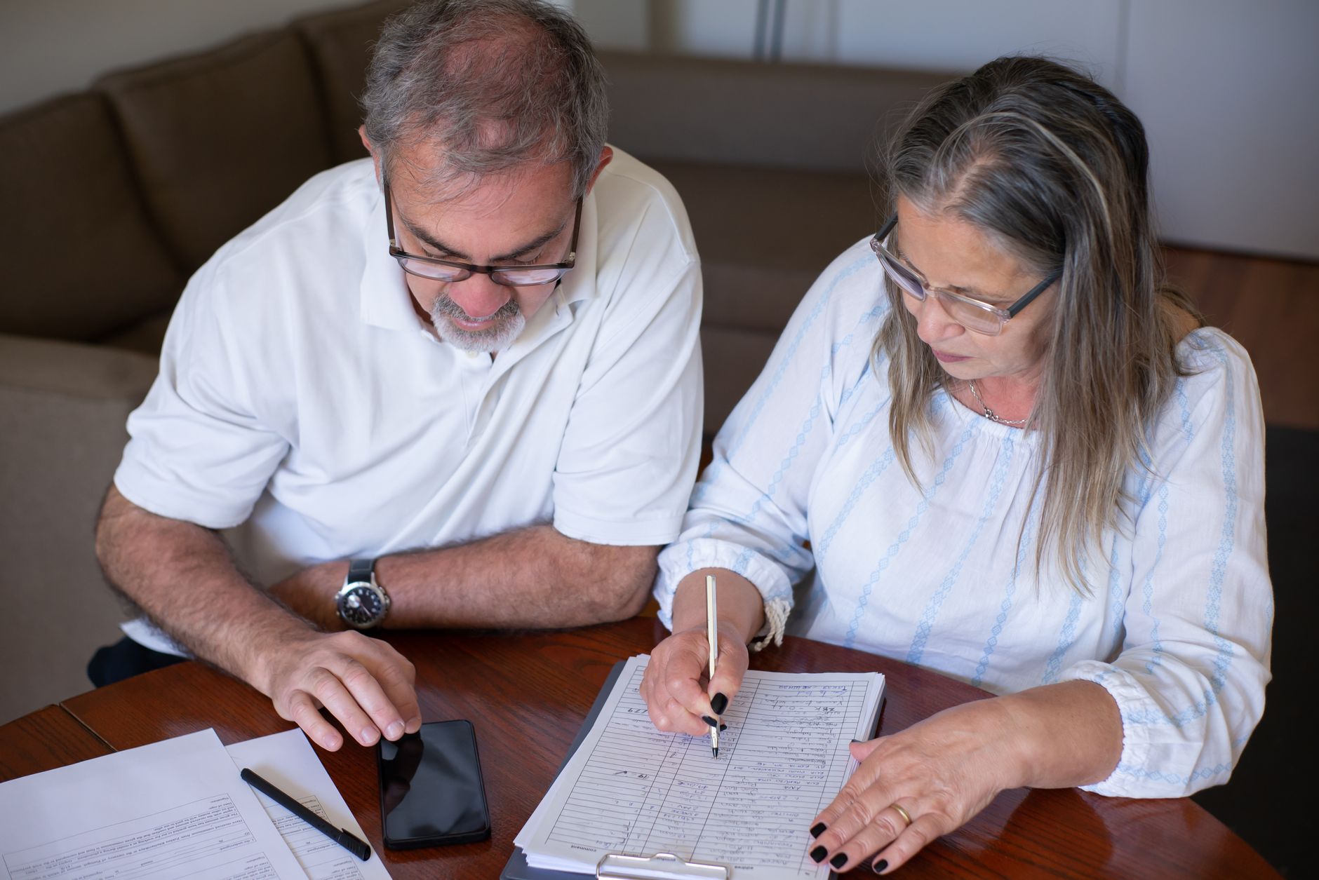 Quem pode fazer empréstimo consignado? Elderly couple reviewing documents, using smartphone for online banking at home.