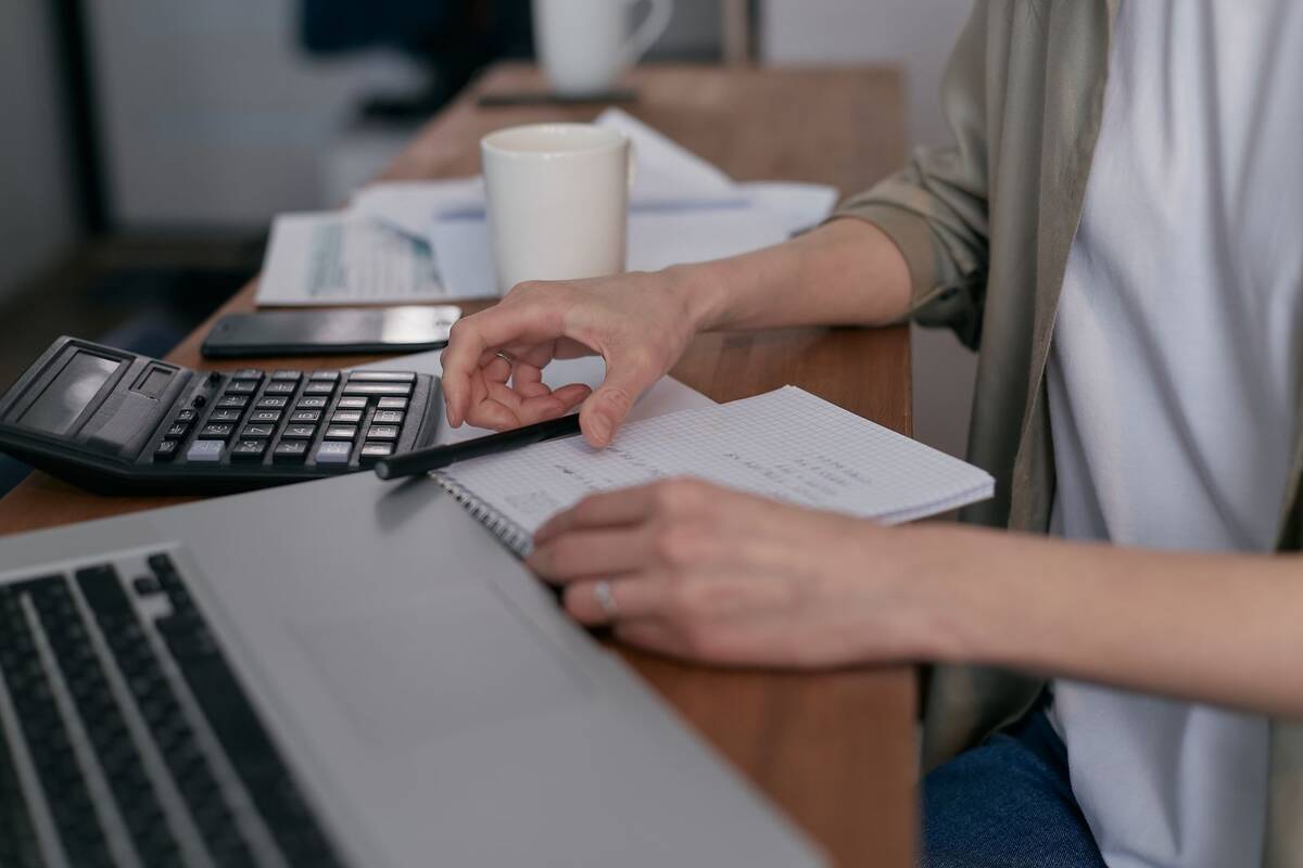 Pessoa calculando as finanças com notebook e bloco de notas