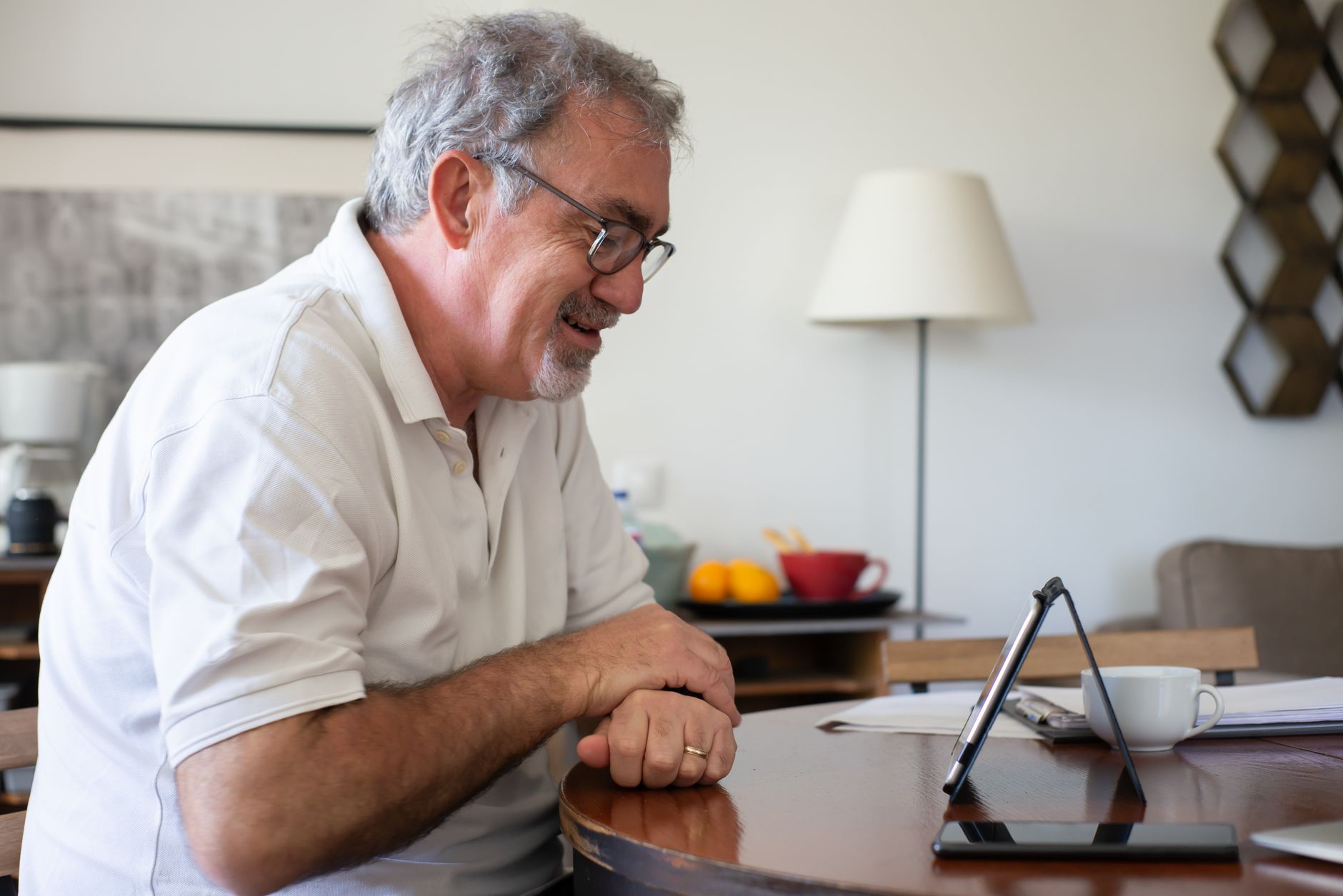 Refinanciamento de consignado: quando vale a pena Elderly man enjoying a video call on a tablet, seated at home with a smile.