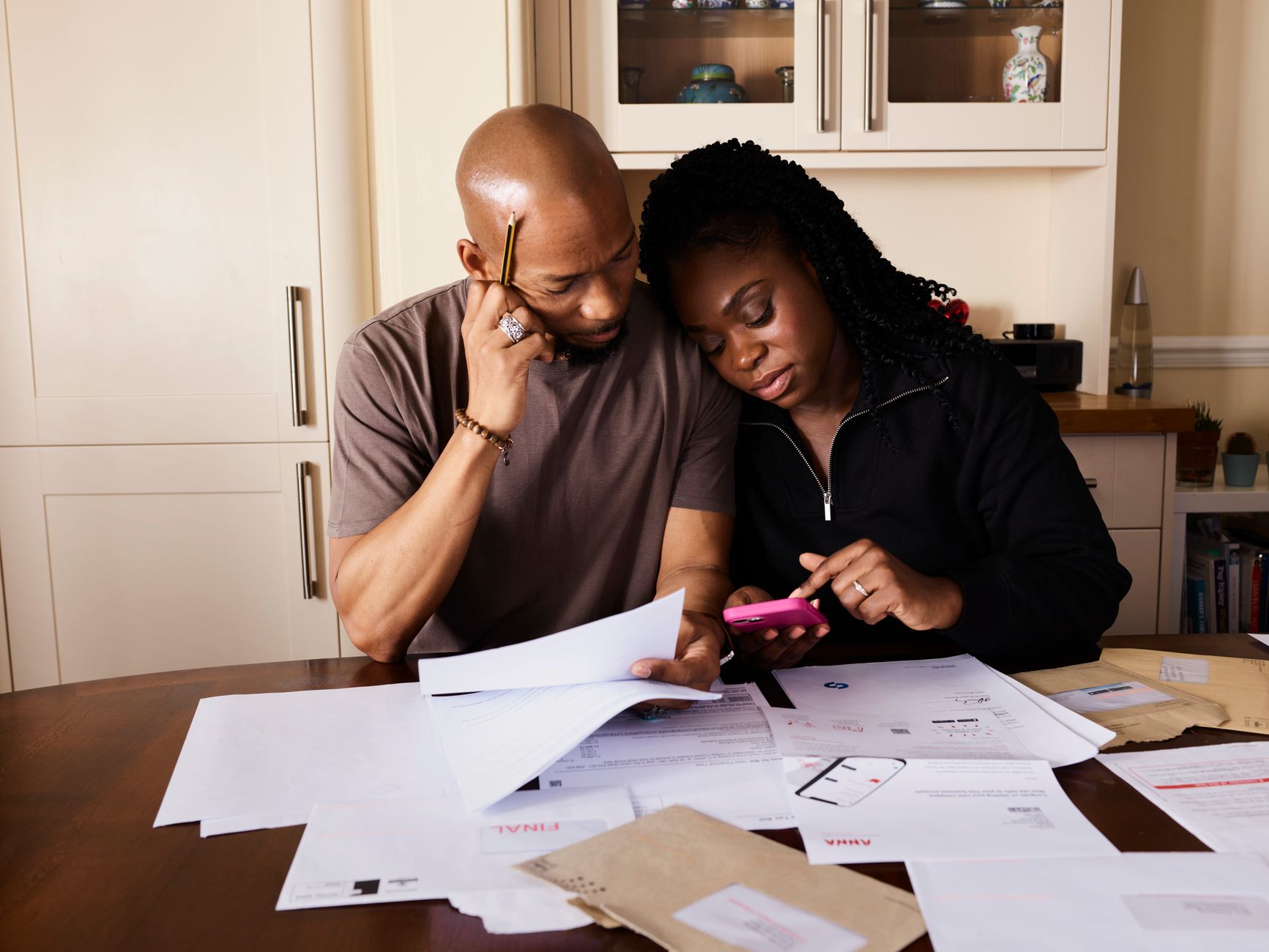 Renegociação de dívida sem juros: quando é possível A couple sits at a table managing domestic finances, evaluating documents and using a smartphone.