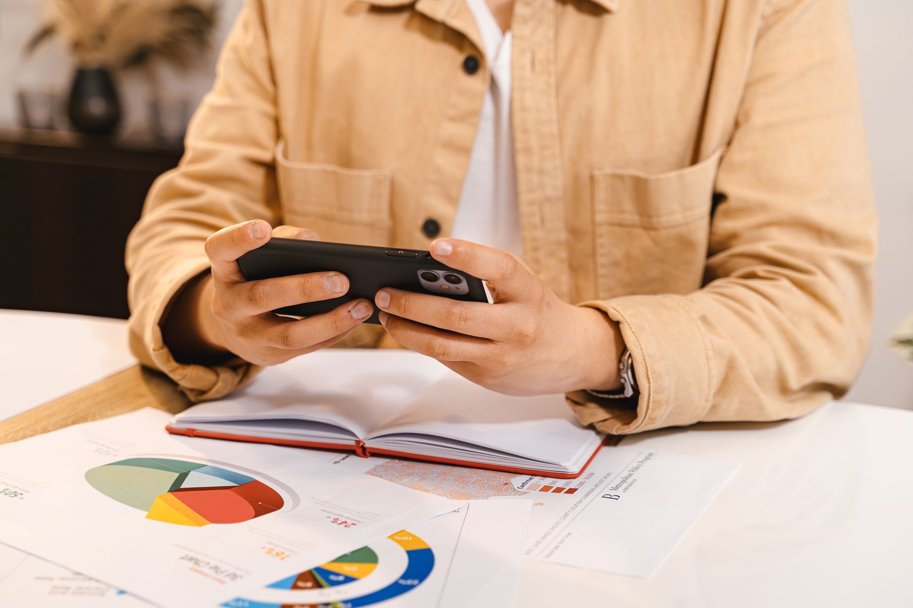 Tenho score alto, mas estou negativado: consigo empréstimo? Person in jacket using smartphone, reviewing charts and data at a workspace.
