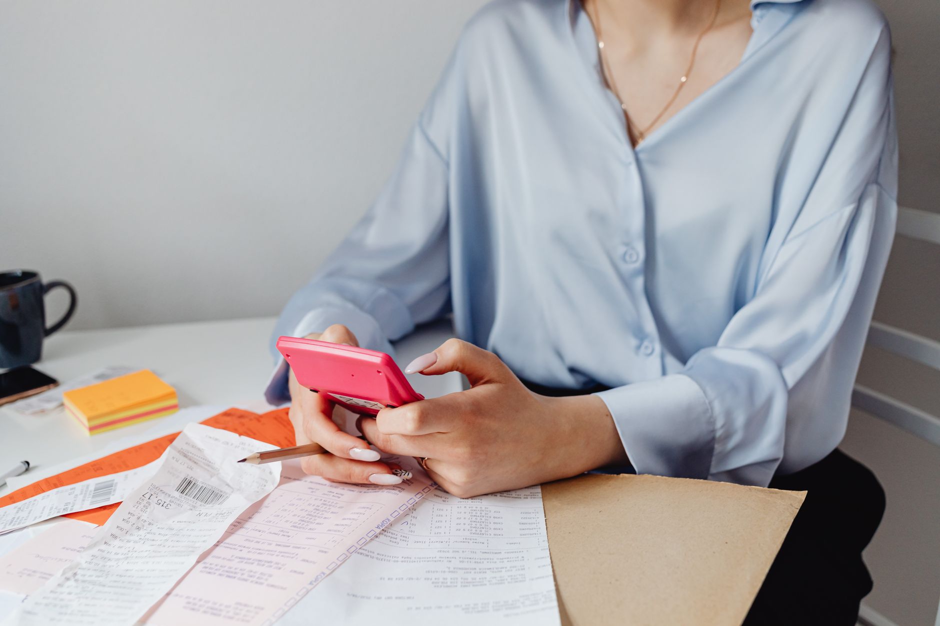 Score zero: o que significa e por que acontece A woman using a pink calculator surrounded by bills and receipts at a desk.