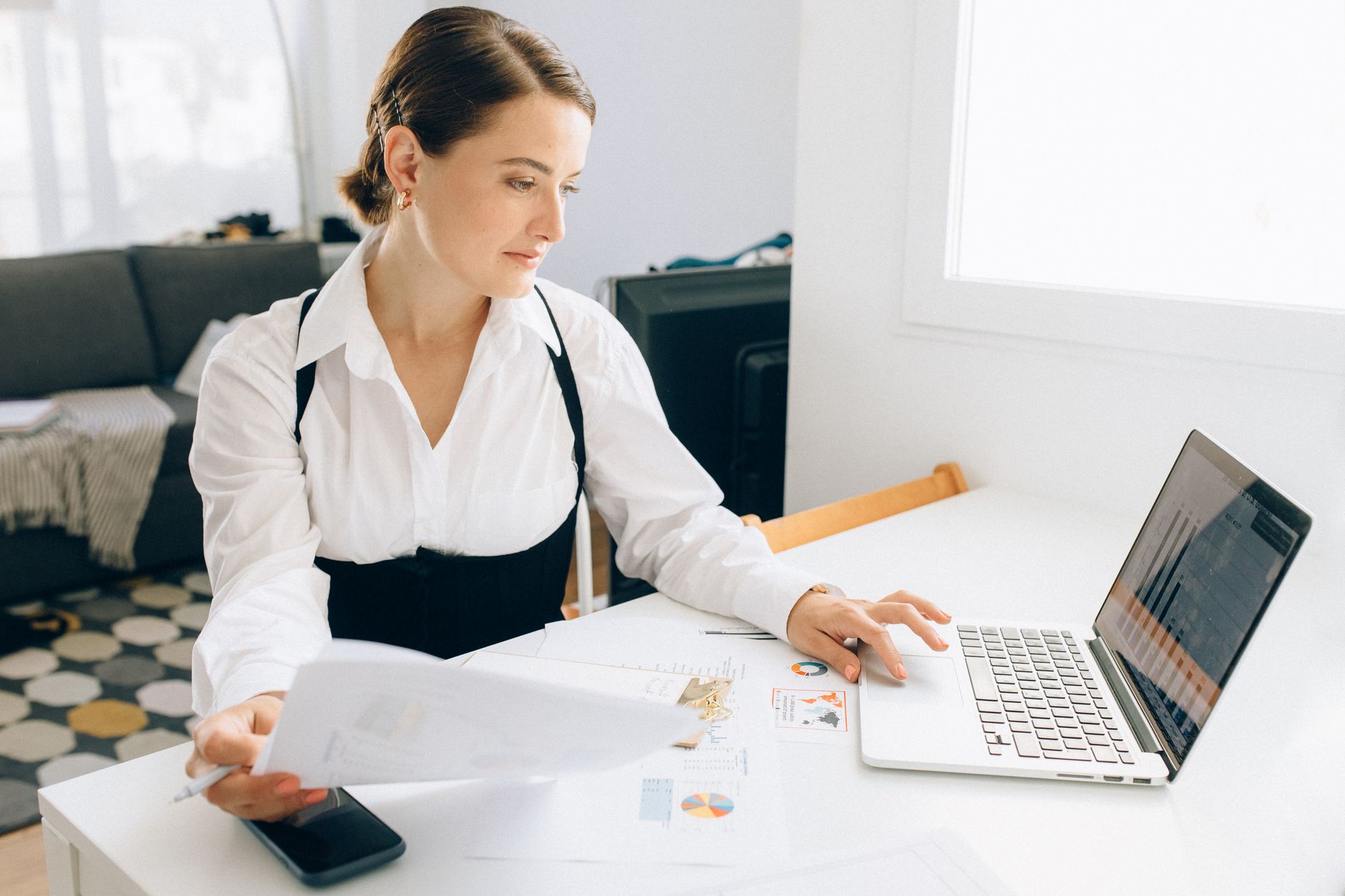 Serasa Premium vale a pena para quem quer crédito? Woman at desk reviewing business reports on laptop, holding papers in a modern office setting.