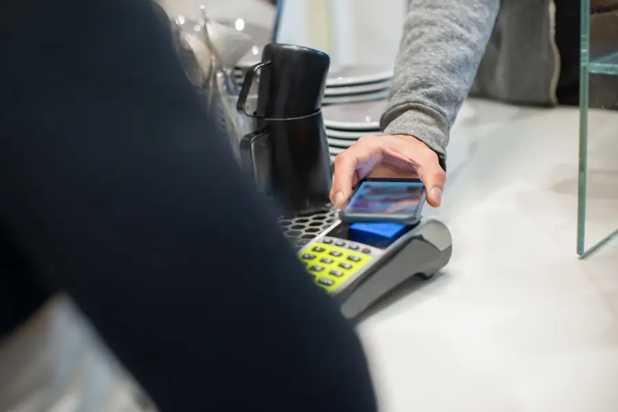 Cliente pagando com o celular por aproximação em uma maquininha de café Cliente pagando com o celular por aproximação em uma maquininha de café