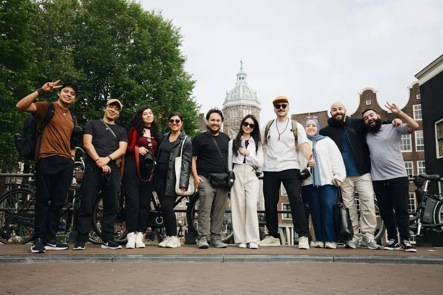 Grupo diverso de turistas posando em Amsterdã diante de um prédio histórico