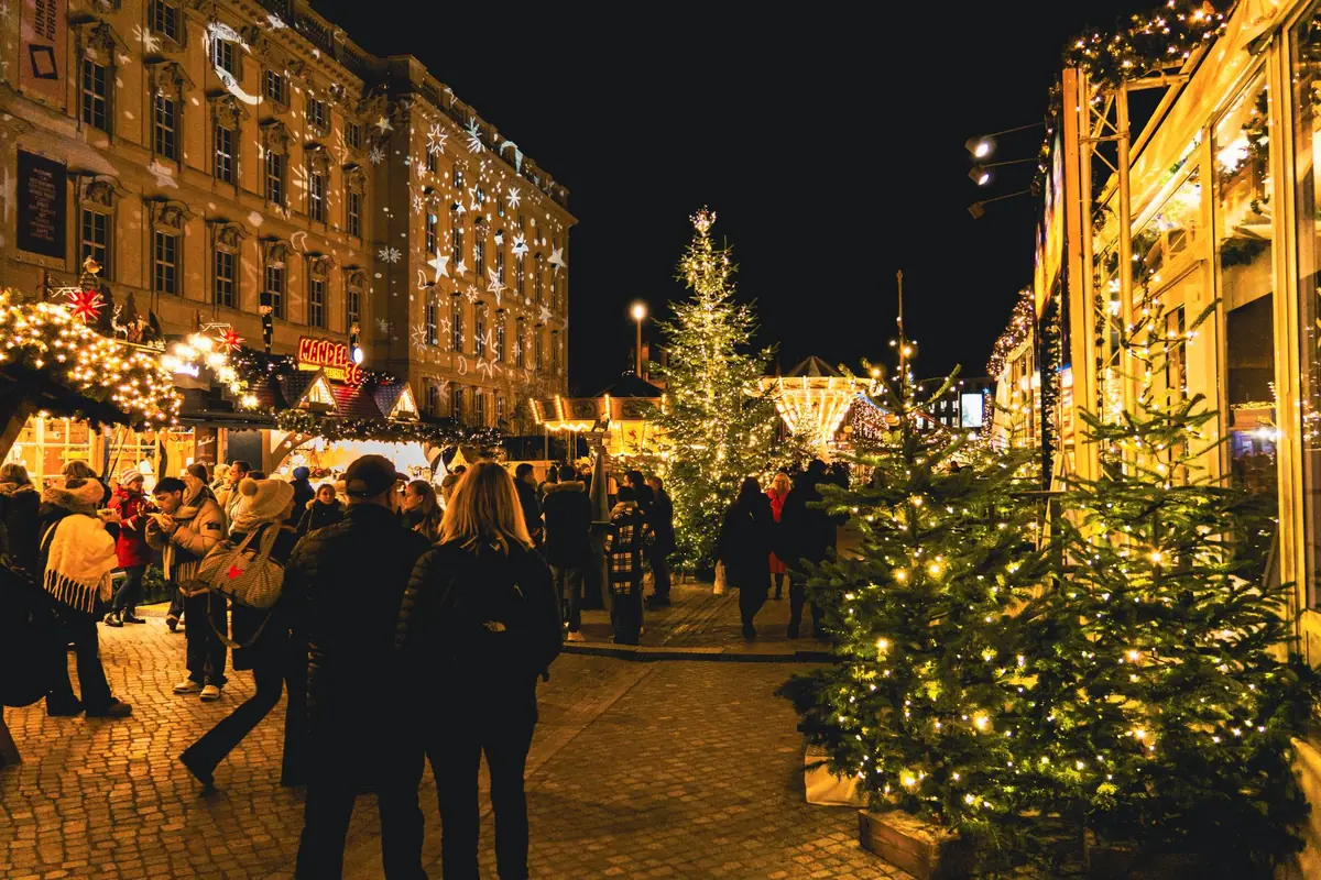 Mercado de Natal à noite com barracas iluminadas e visitantes