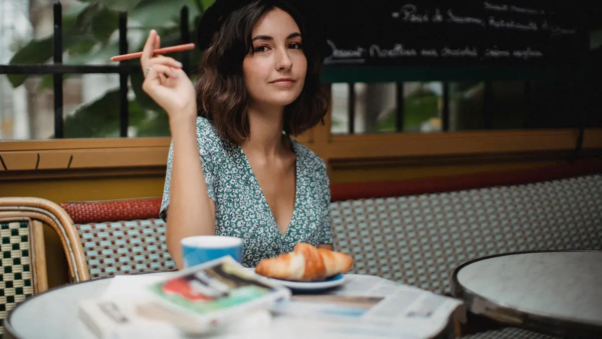 Mulher tomando café com croissant em uma mesa ao ar livre de um café europeu