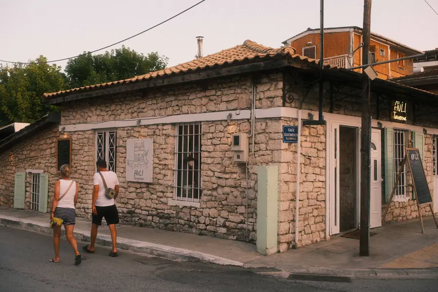 Casal caminhando diante de uma taverna de pedra em Lefkada, na Grécia Casal caminhando diante de uma taverna de pedra em Lefkada, na Grécia