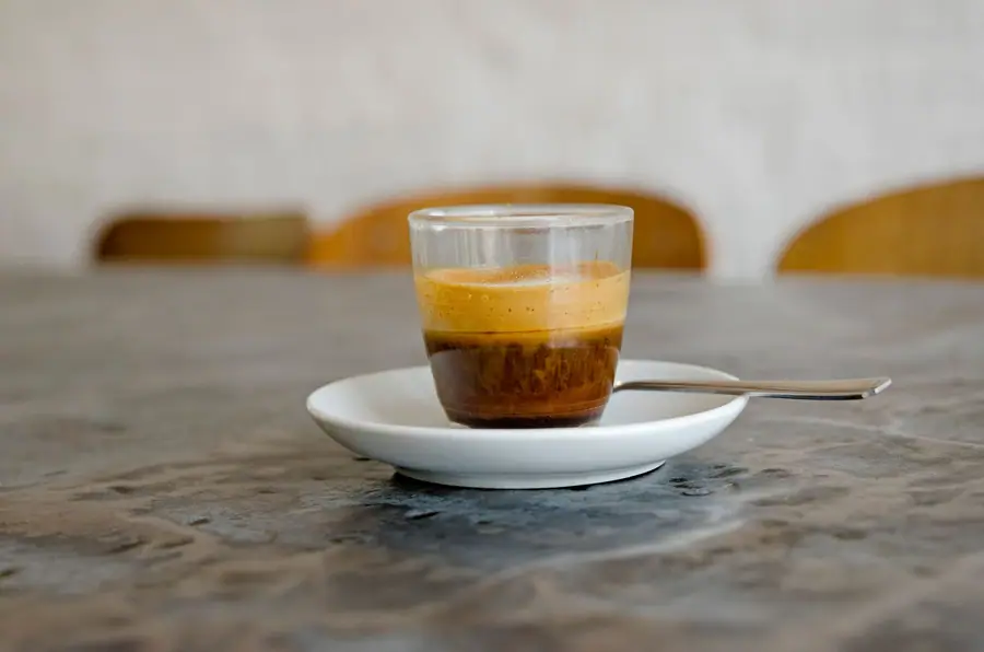 Close de um café expresso em xícara de vidro sobre um pires