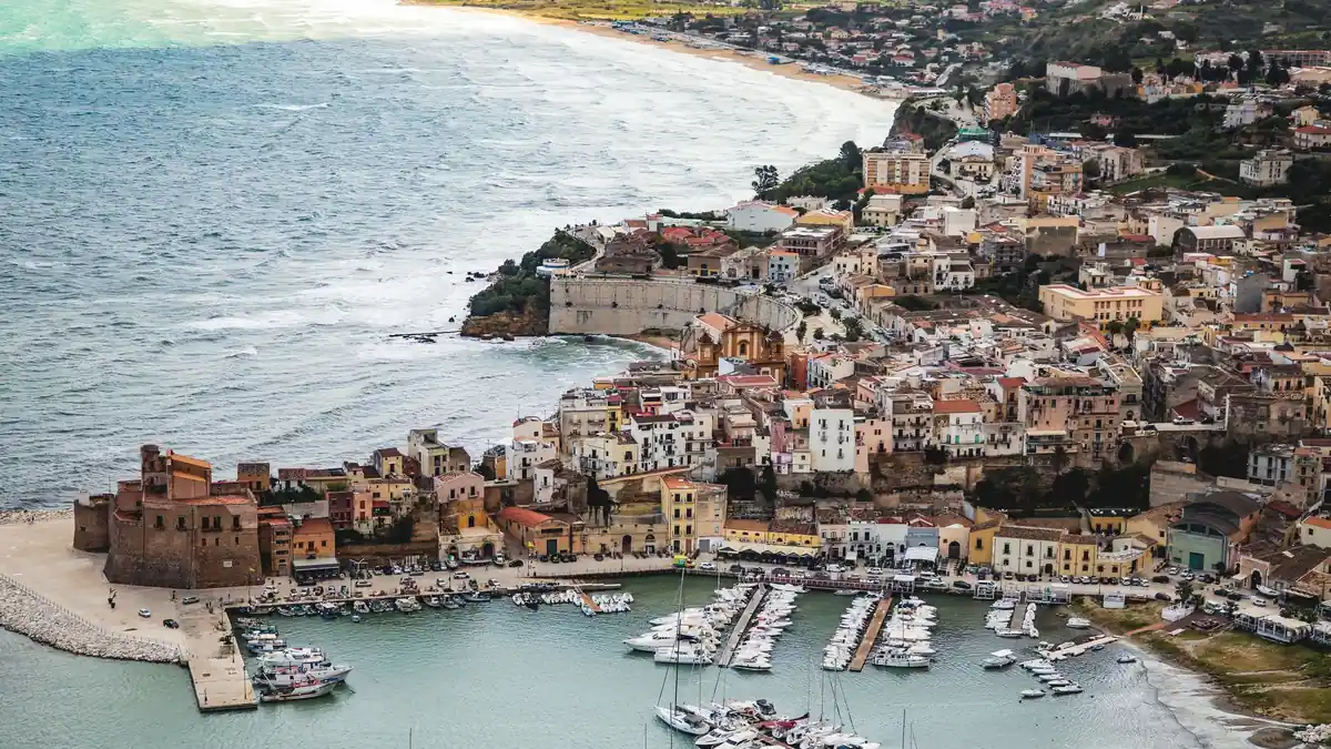 Cidade costeira da Sicília com marina e prédios históricos à beira-mar
