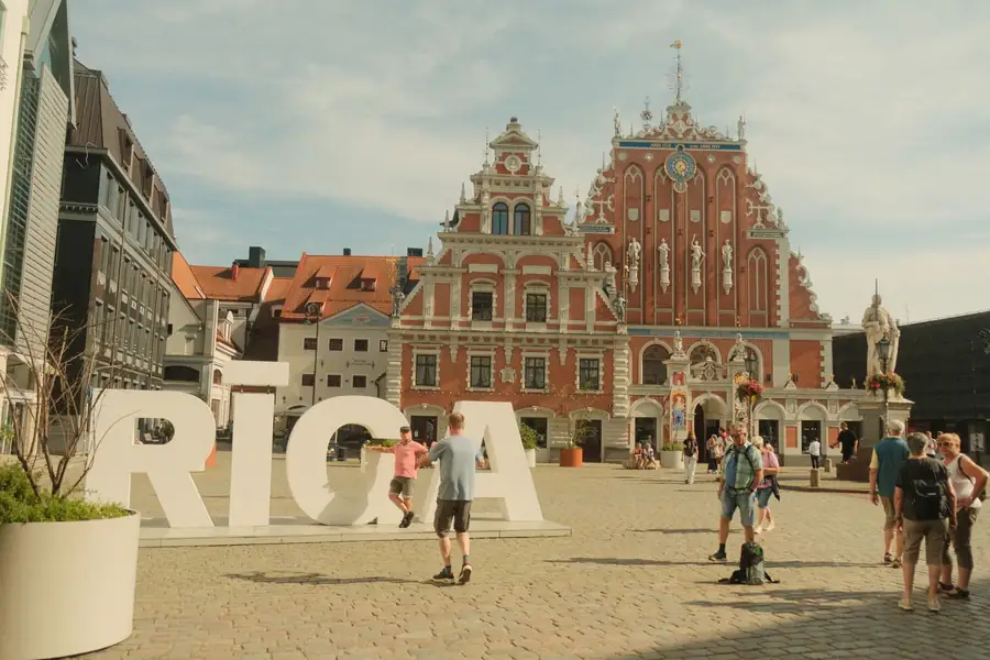 Pessoas passeando na Praça da Prefeitura de Riga com a Casa dos Cabeças Negras
