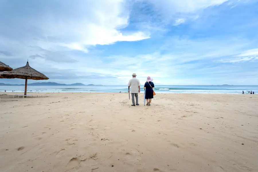 Casal de idosos caminhando em uma praia sob um céu azul Casal de idosos caminhando em uma praia sob um céu azul