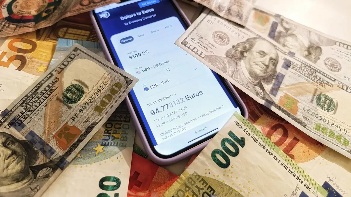 Celular exibindo um conversor de moedas cercado por notas de dólar e euro