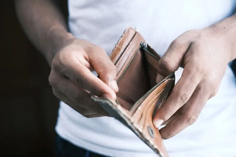 Mãos segurando uma carteira vazia, símbolo de crise financeira