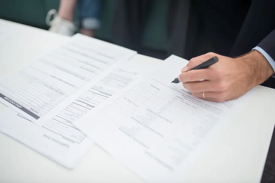 Mão assinando um documento de seguro sobre uma mesa de escritório Mão assinando um documento de seguro sobre uma mesa de escritório