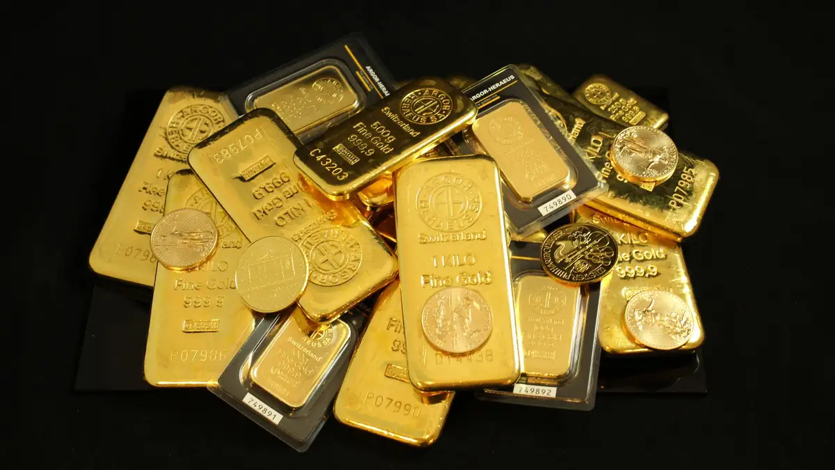Barras de ouro e moedas sobre fundo escuro simbolizando proteção de patrimônio