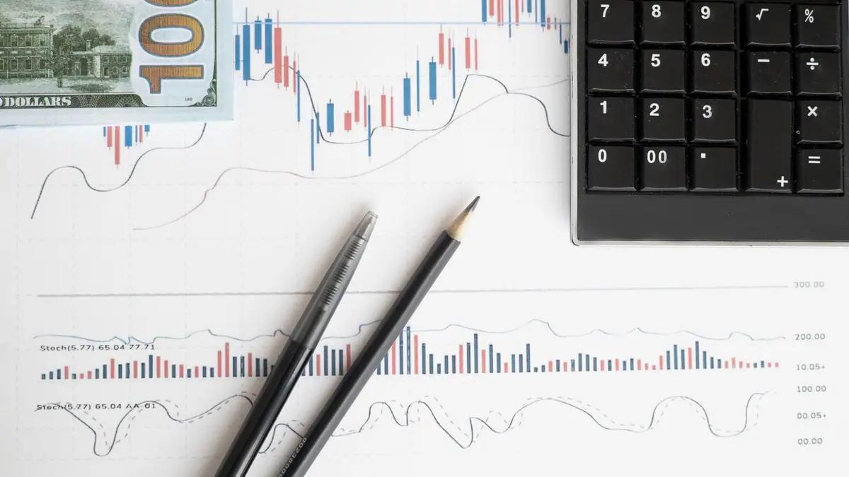 Mesa de trabalho com calculadora, gráficos e moedas usada em análise de ações